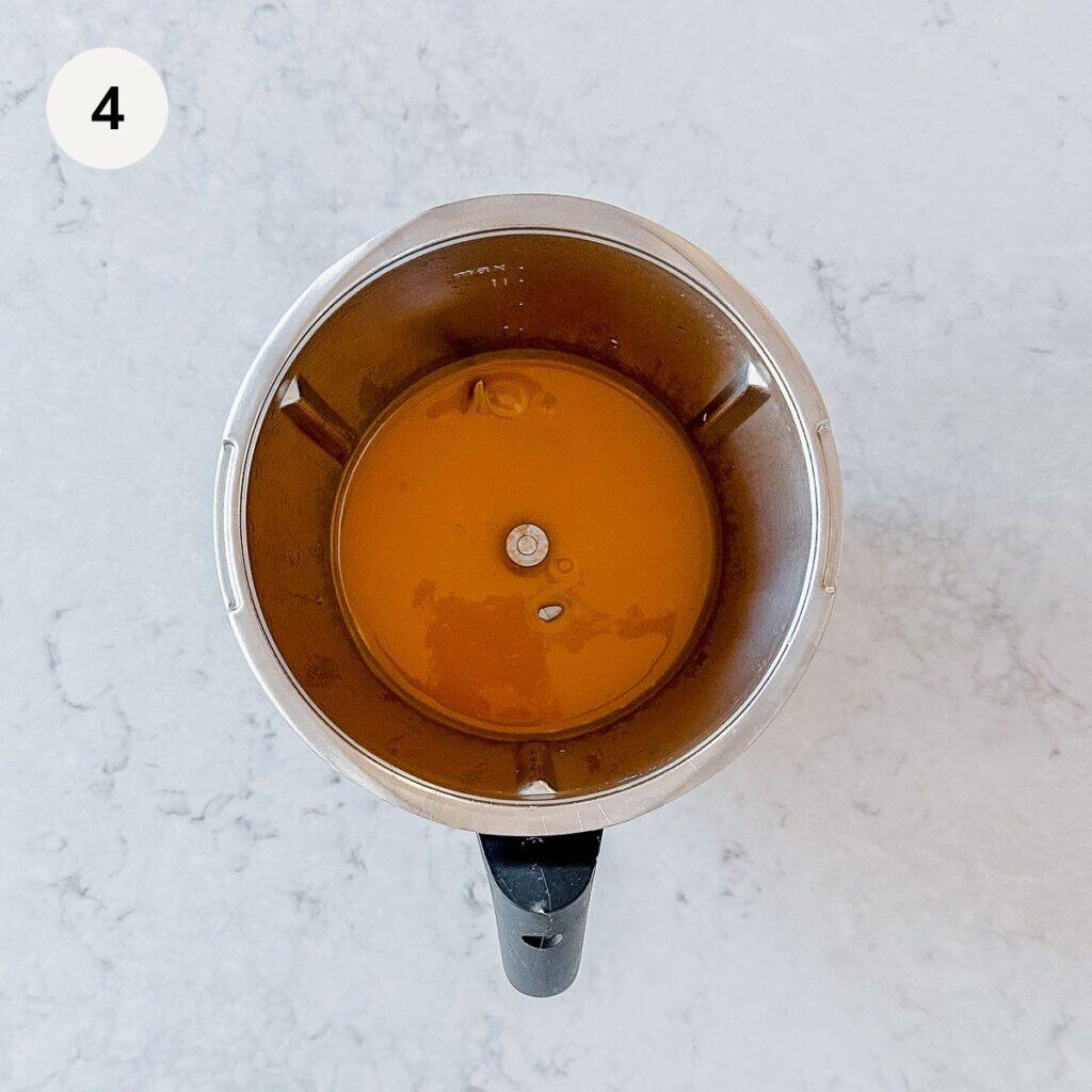 A blender viewed from above, filled with caramel on a light marbled surface. A black handle is visible at the bottom. The number 4 is in a white circle in the top left corner.