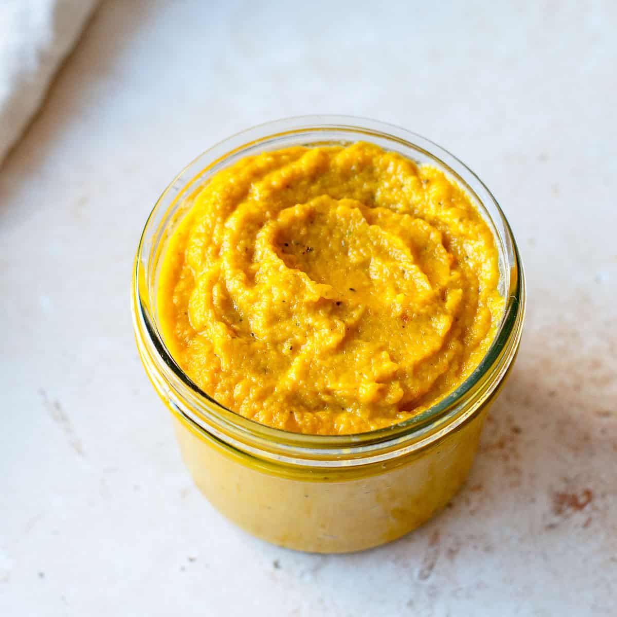 Homemade vegetable stock paste in a glass jar on a light background.