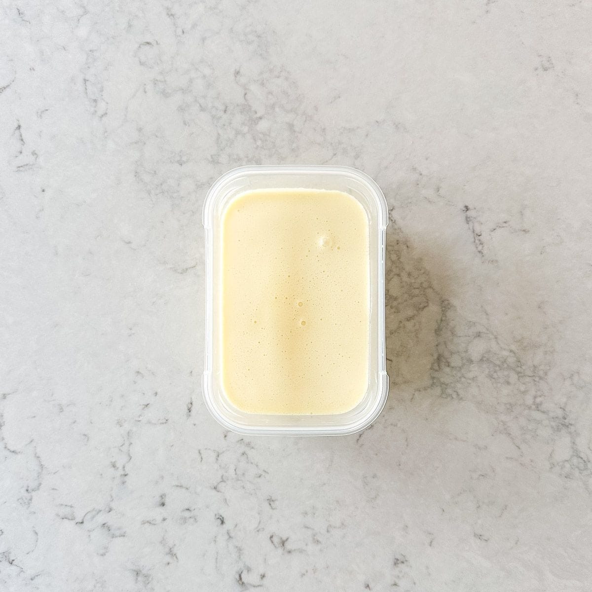 sweetened condensed milk in a rectangle container on a grey marble benchtop.