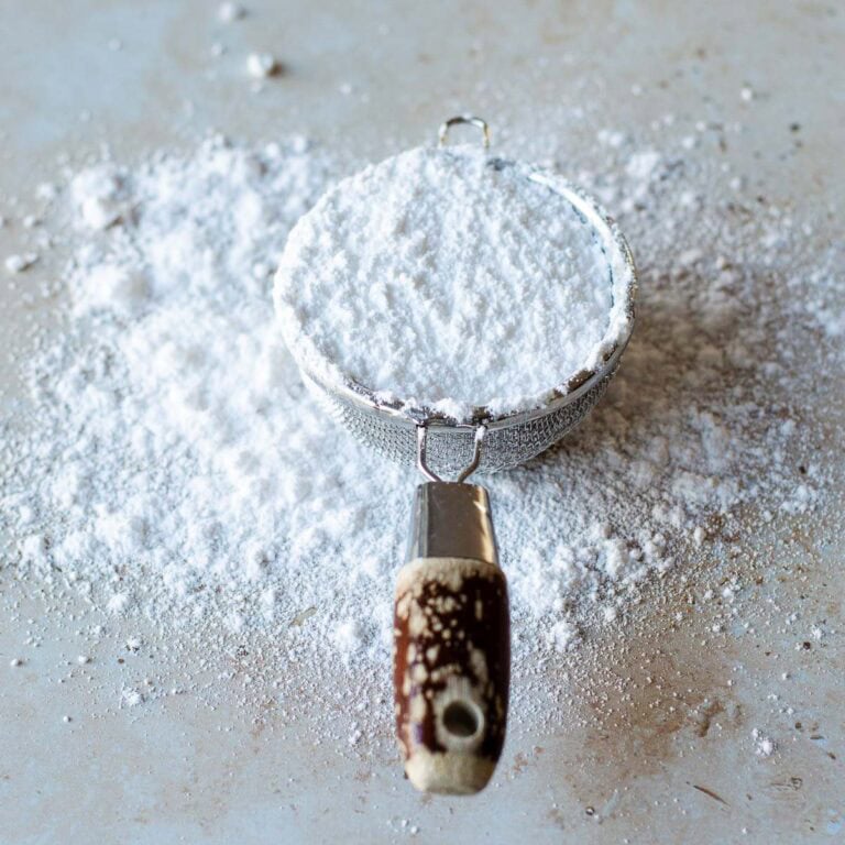 Icing sugar in a sieve on a stone benchtop.