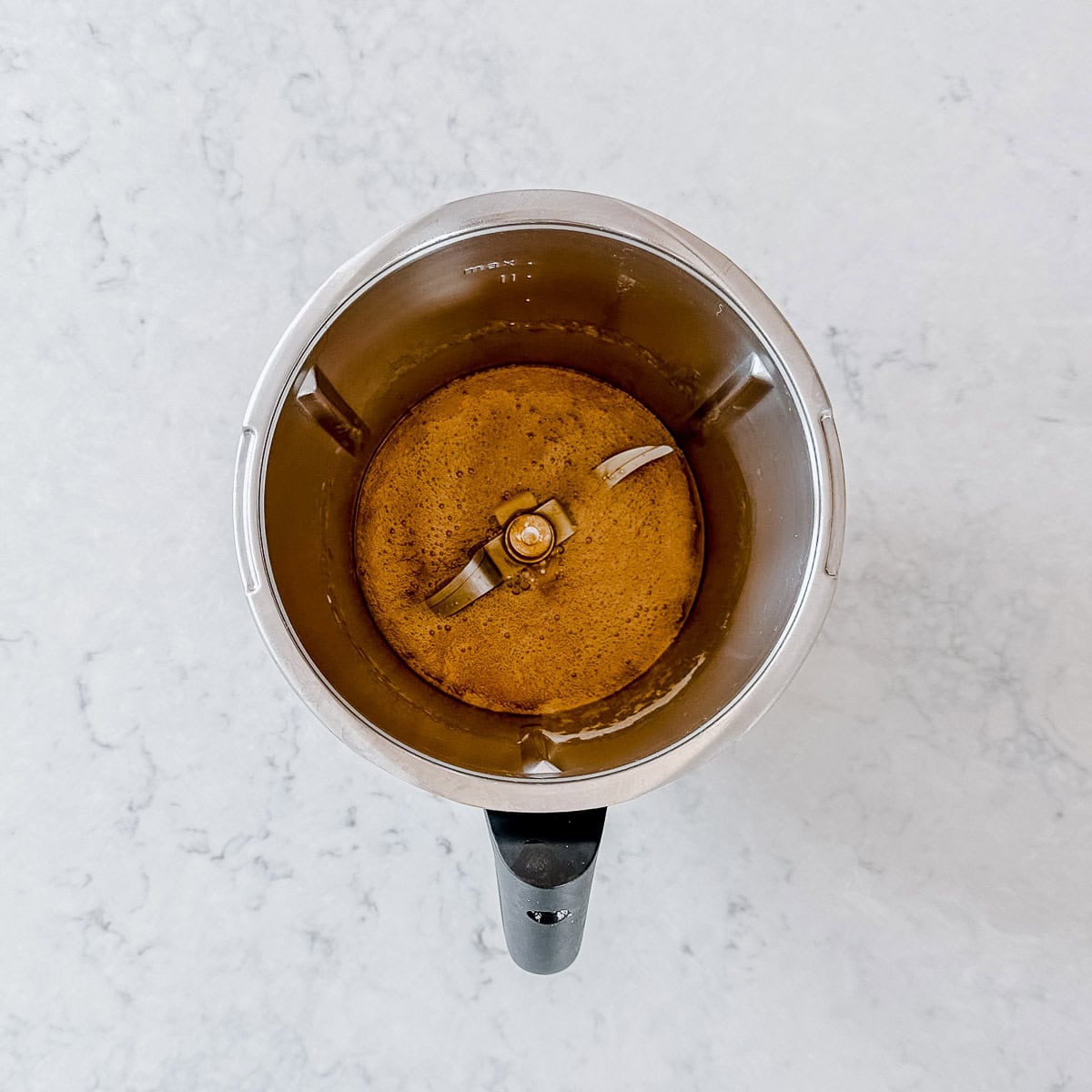 Caramel sauce in a Thermomix bowl, on a grey marble benchtop.