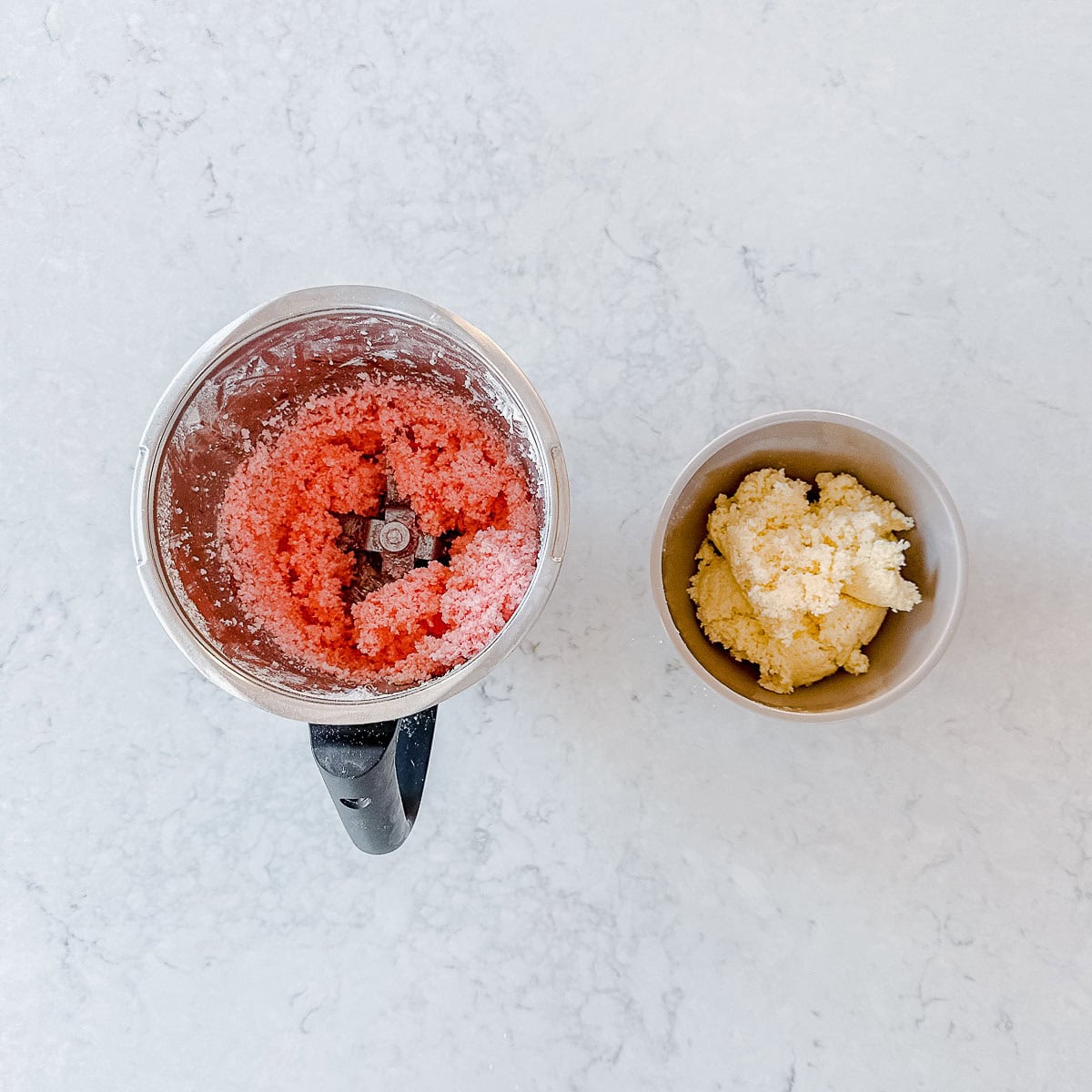An overhead image of a Thermomix bowl with pink coconut ice mixture sitting next to a bowl with white coconut ice mixture.