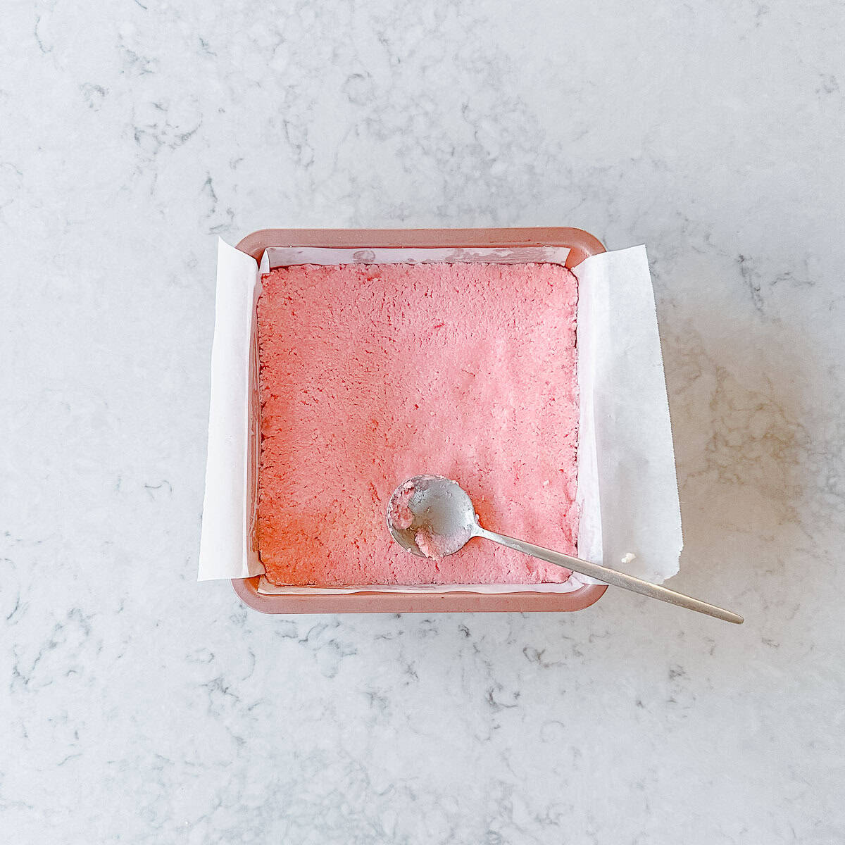 Pink coconut Ice in a square baking tin, smoothed over the top with a spoon.