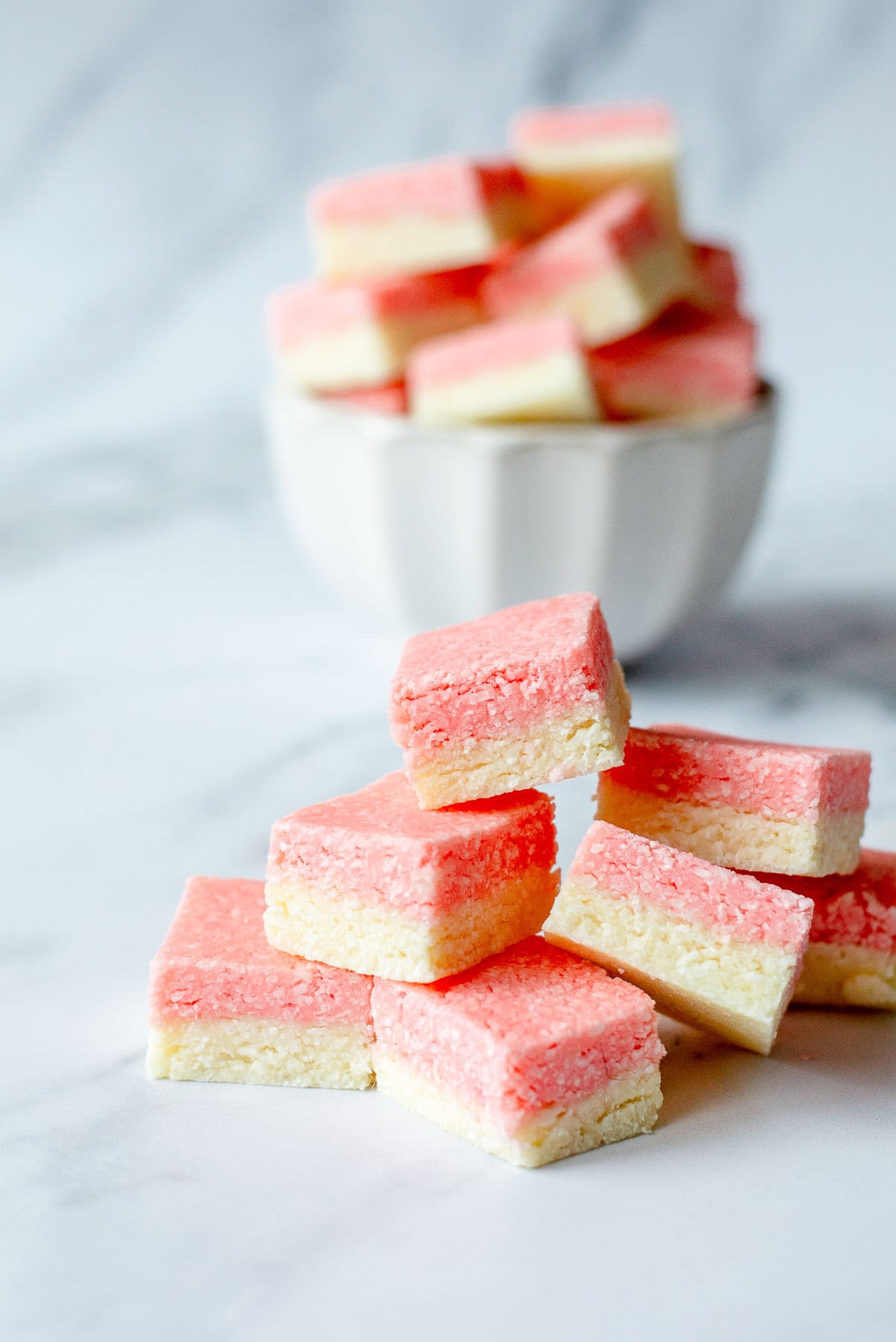 Squares of pink and white coconut ice stacked on a marble benchtop.
