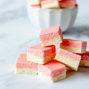 Squares of pink and white coconut ice stacked on top of each other, on a marble benchtop.