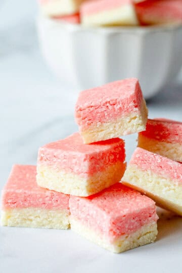 Squares of pink and white coconut ice stacked on top of each other, on a marble benchtop.