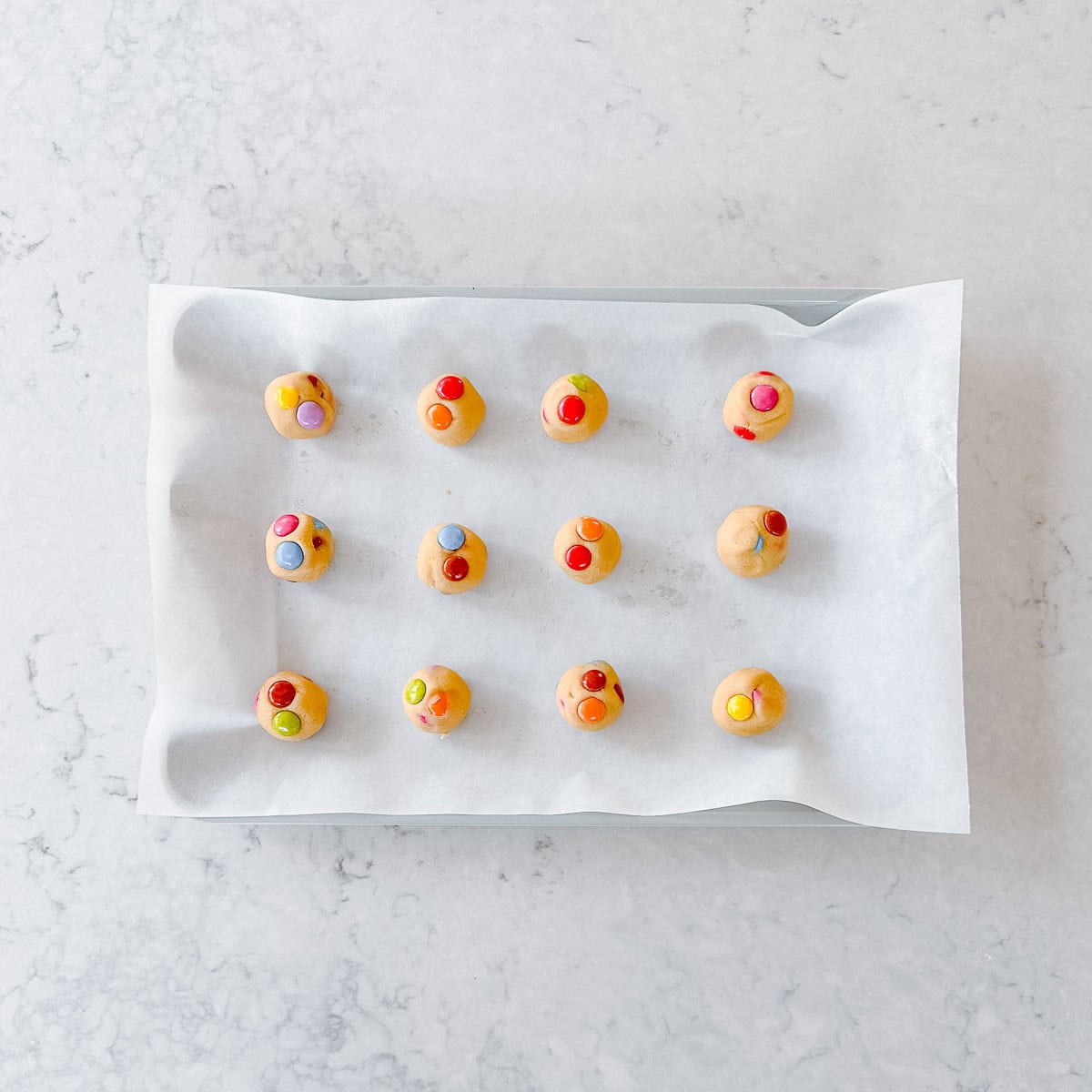 Smartie cookie dough balls on a baking sheet lined with baking paper.