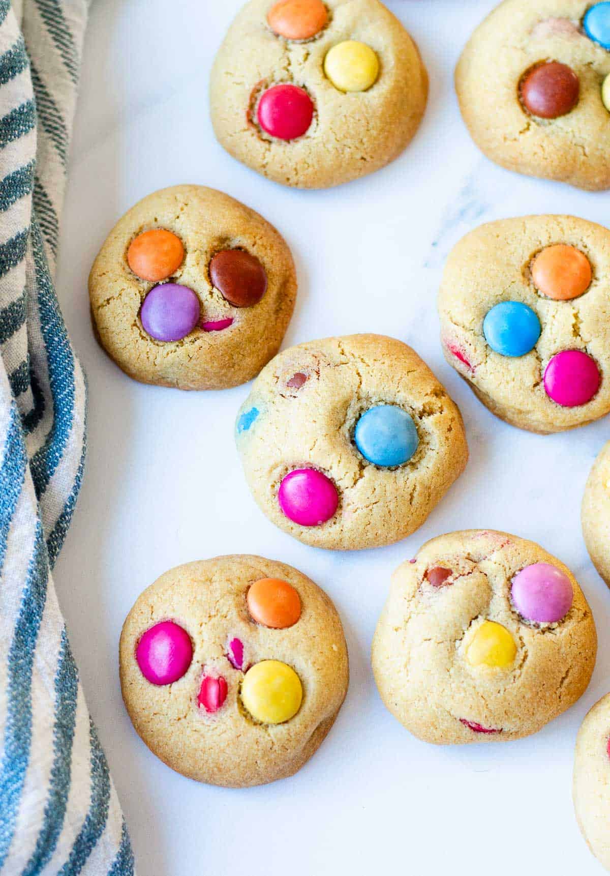 Smartie Cookies on a white marble benchtop, with a blue striped tea towel on the left.
