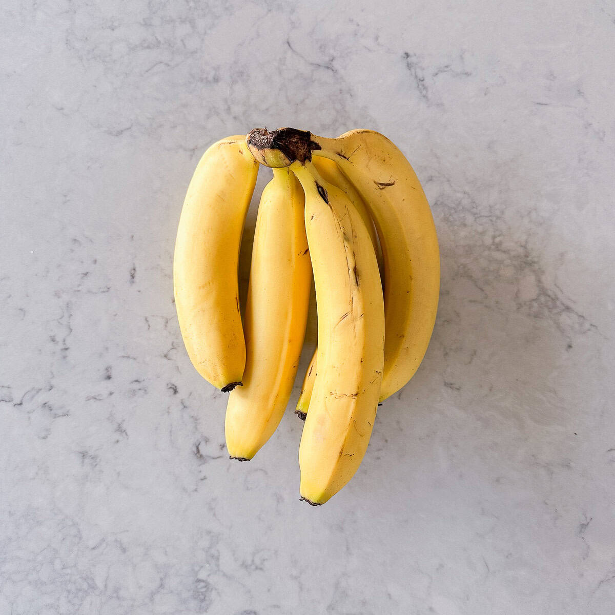 A bunch of bananas on a grey marble benchtop.