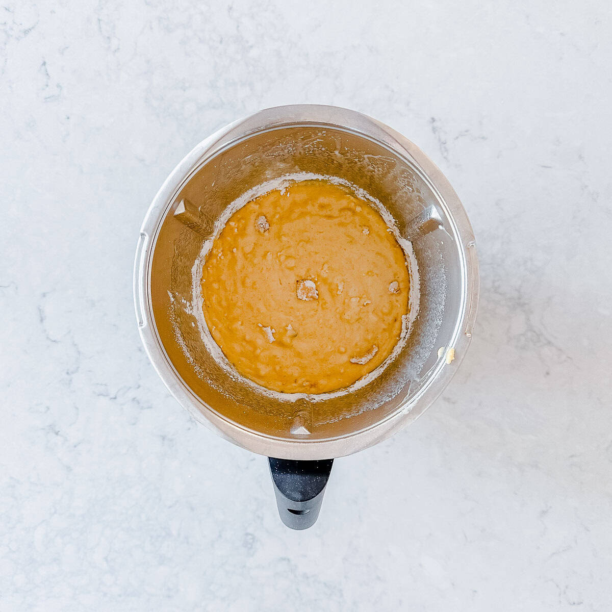 Overhead view of the finished banana bread batter in a Thermomix bowl, showing a thick, lumpy texture after mixing.