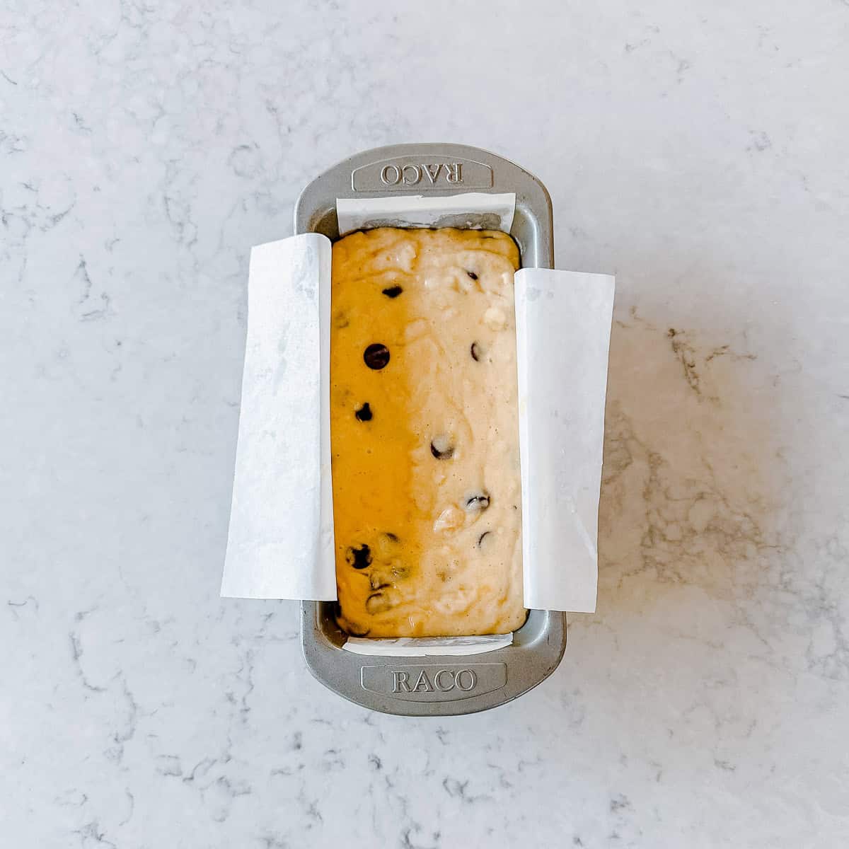 Overhead view of chocolate chip banana bread batter poured into a baking paper-lined loaf tin, ready to go into the oven.