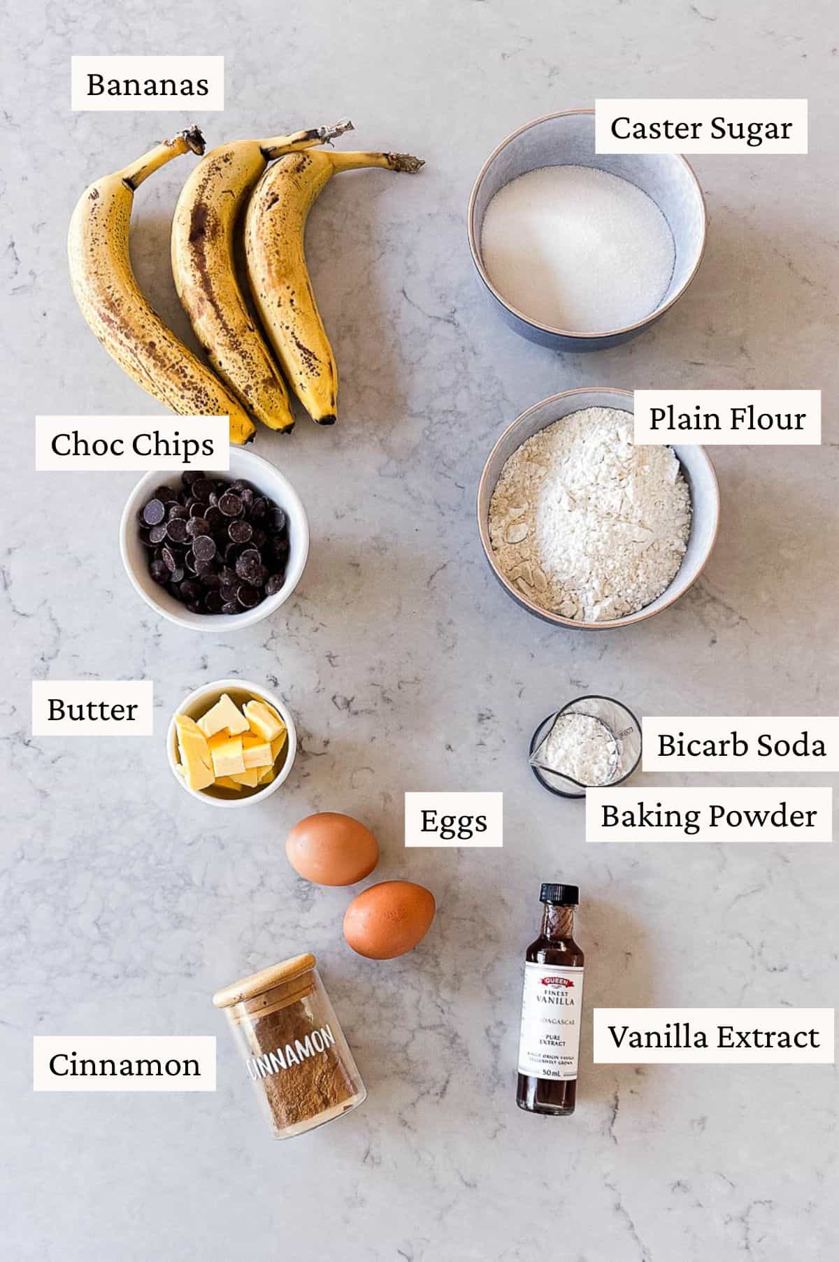 Overhead flatlay of ingredients need to make chocolate chip banana bread. All the ingredients are labelled.