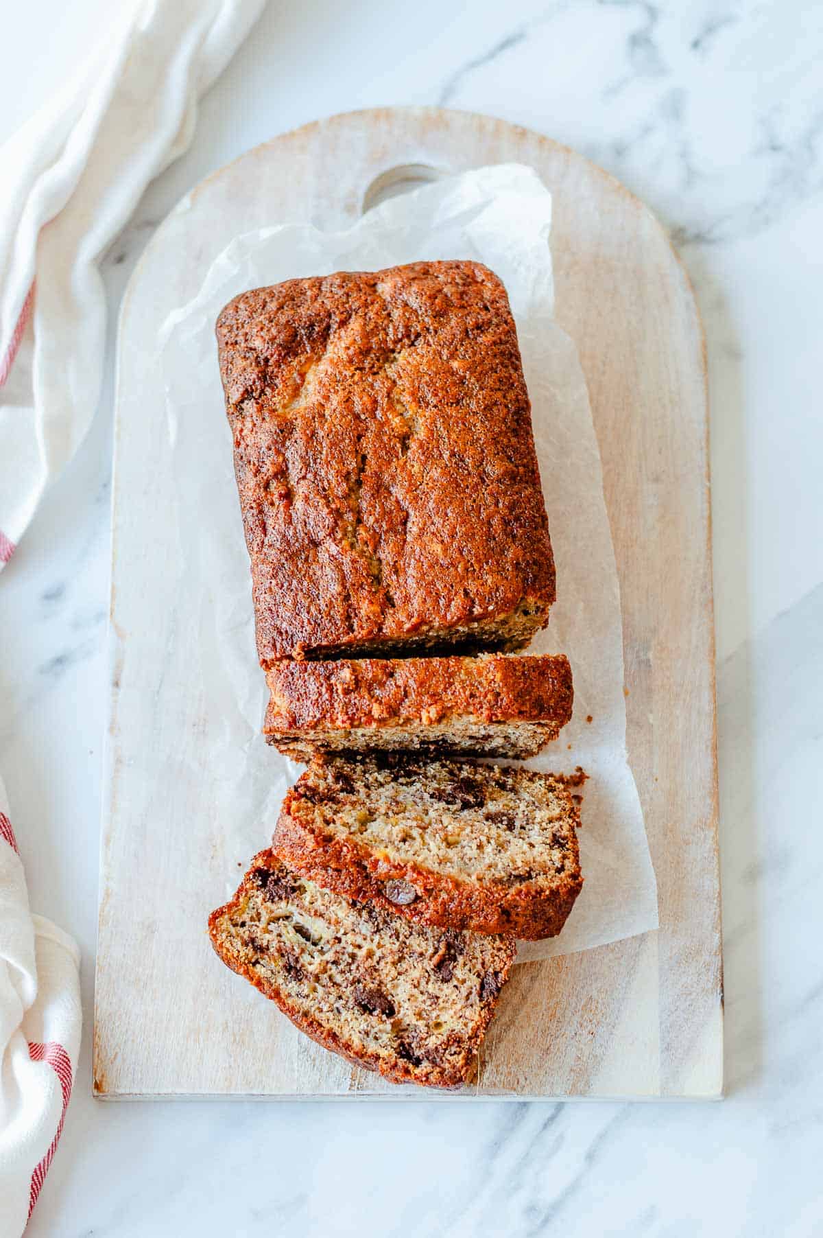 Overhead view of chocolate chip banana loaf sliced on a wooden board with dark chocolate chips throughout.