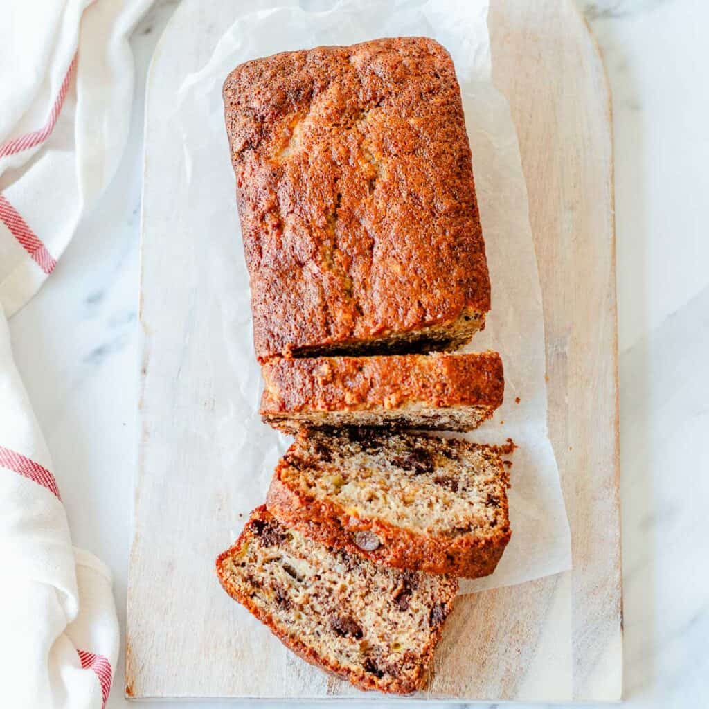 Overhead view of chocolate chip banana bread loaf sliced on a wooden board with dark chocolate chips throughout.