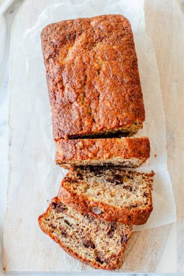 Overhead view of chocolate chip banana bread loaf sliced on a wooden board with dark chocolate chips throughout.