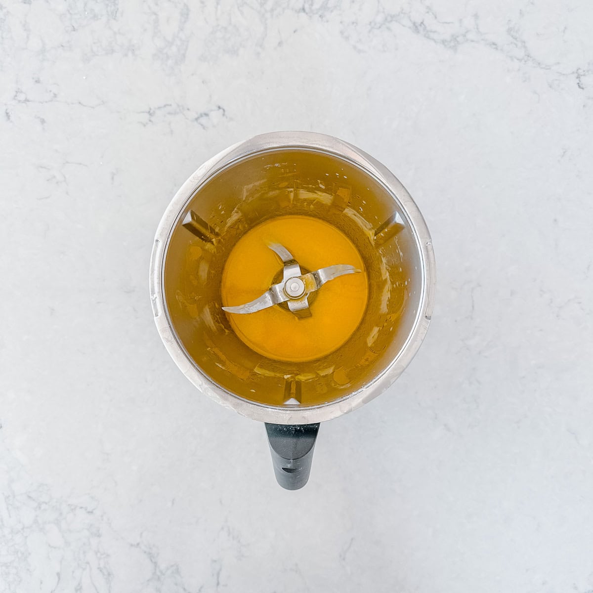 Top view of a Thermomix jug containing melted butter, on a light marble surface.