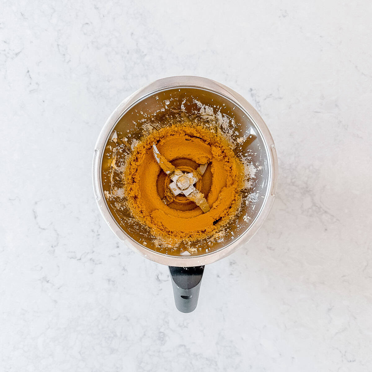A top-down view of a blender containing creamed brown sugar on a light marbled surface.