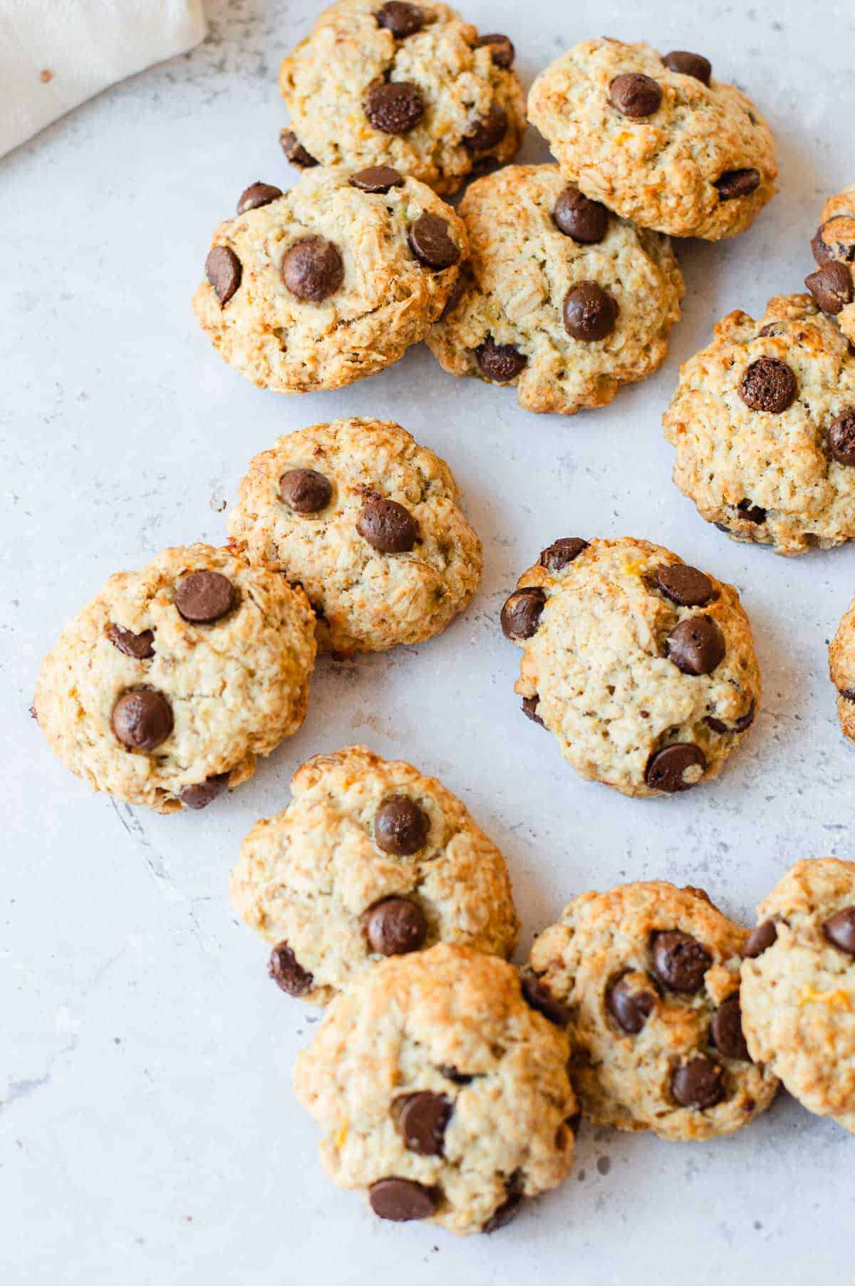 A batch of freshly baked chocolate chip biscuits is arranged on a light-coloured surface, showcasing their golden-brown texture and visible chocolate chips.